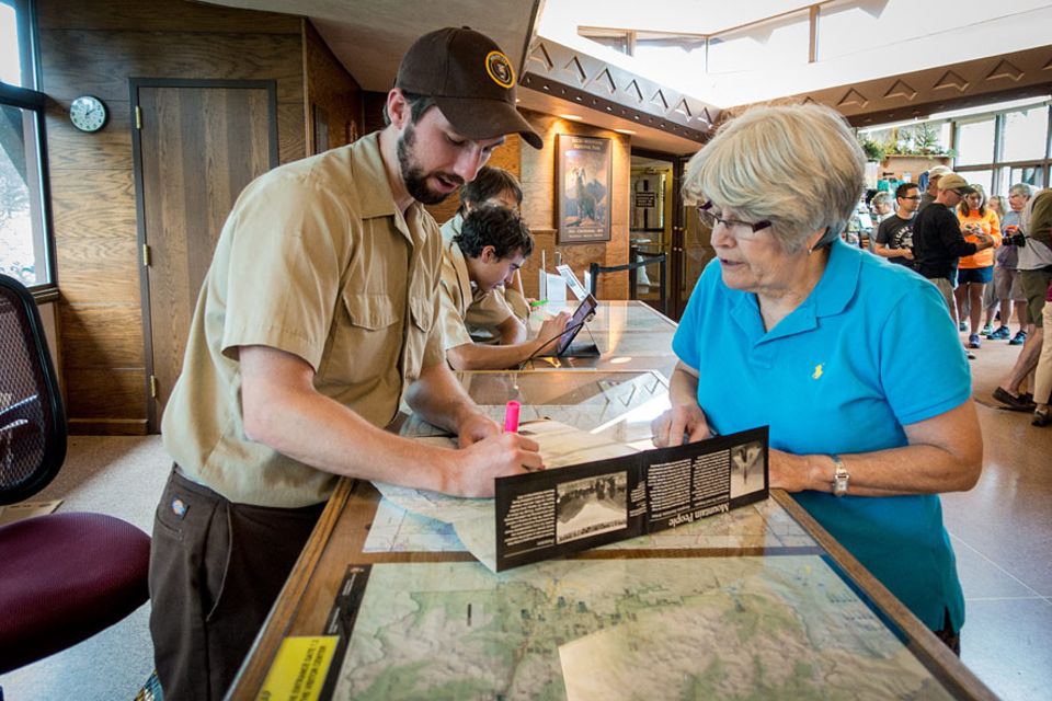 Rocky Mountains Nationalpark: Ein Ranger markiert auf einer Landkarte für eine Besucherin empfohlene Haltepunkte im Rocky Mountain Nationalpark