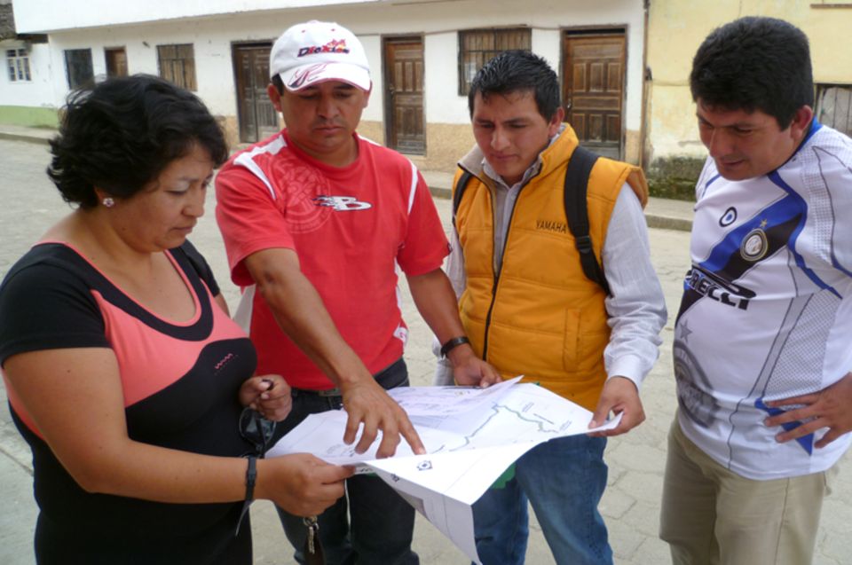 Silvia Quilumbango und Armando Almeida von DECOIN sowie zwei potentielle Verkäufer studieren eine Karte, auf der eine zum Verkauf angebotene Waldfläche verzeichnet ist