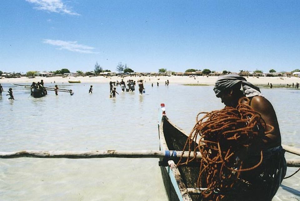 Eine Vezo-Frau beim Entladen eines Bootes. Im Hintergrund sieht man Anakao und das gesellige Treiben am Ende des Tages, wenn der Fischfang vollendet ist.