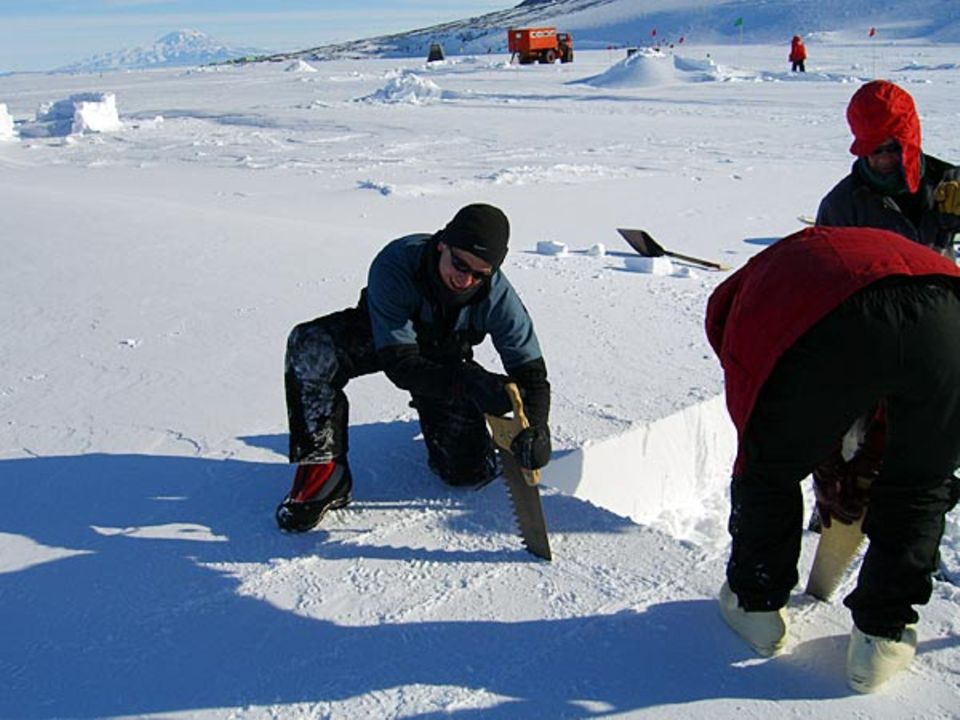 Aus dem vom Wind steinhart planierten Schneeboden sägt GEO-Redakteru Lars Abromeit passgenaue Blöcke für eine Schutzmauer heraus