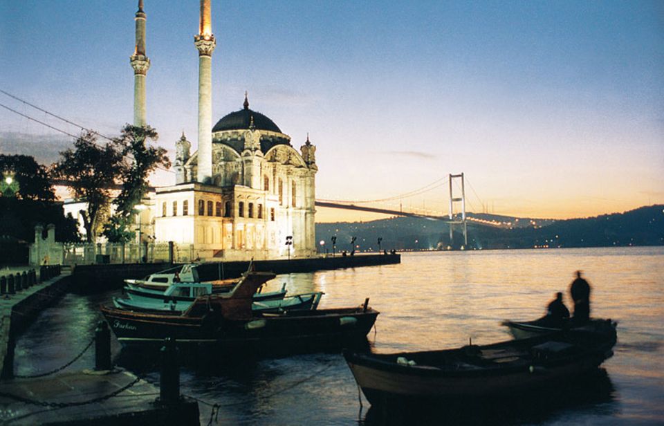 Am Bosporus erhebt sich die Ortaköy-Moschee, die Brücke im Hintergrund verbindet Europa mit Asien. Fischer kehren in ihren Booten zurück - Idylle mitten in Metropolis