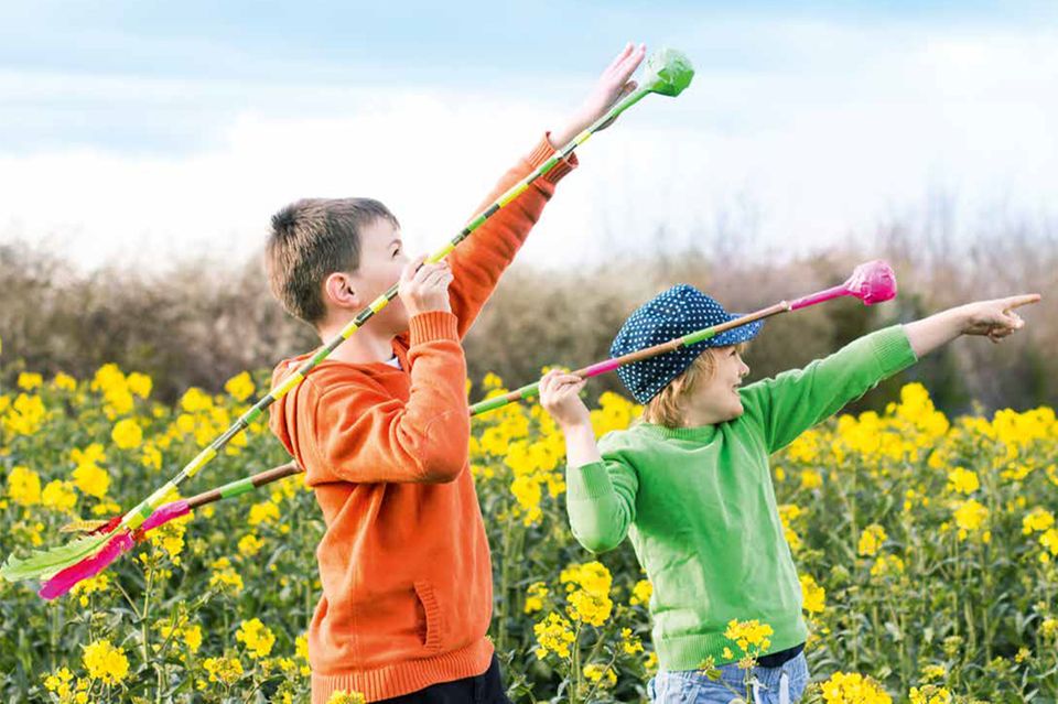 Kinder werfen auf einer Wiese Wurfspeere aus Ästen