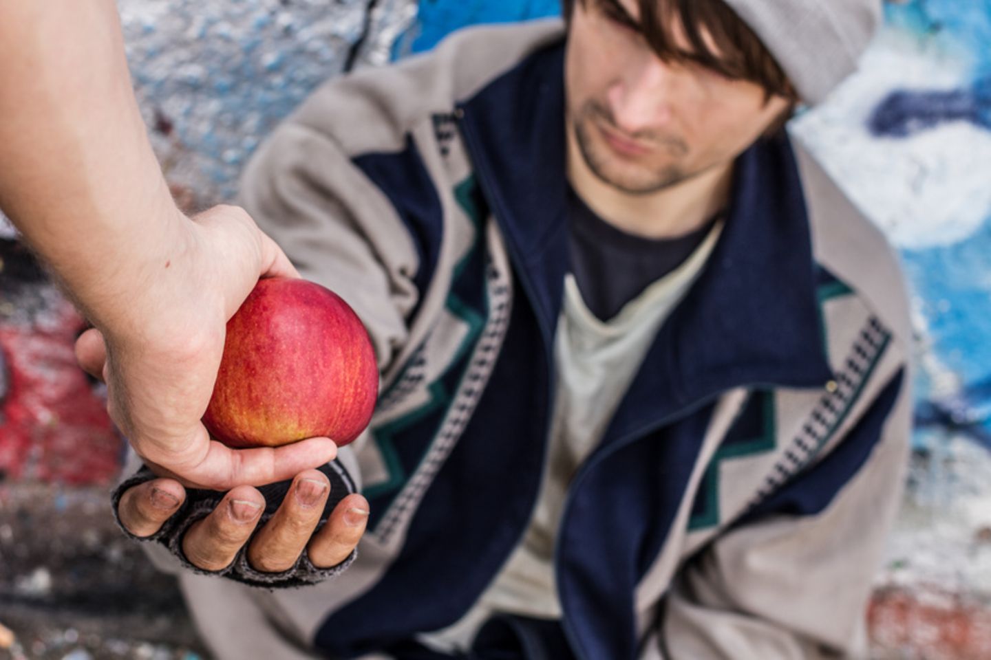 Obdachloser Mensch bekommt einen Apfel gereicht