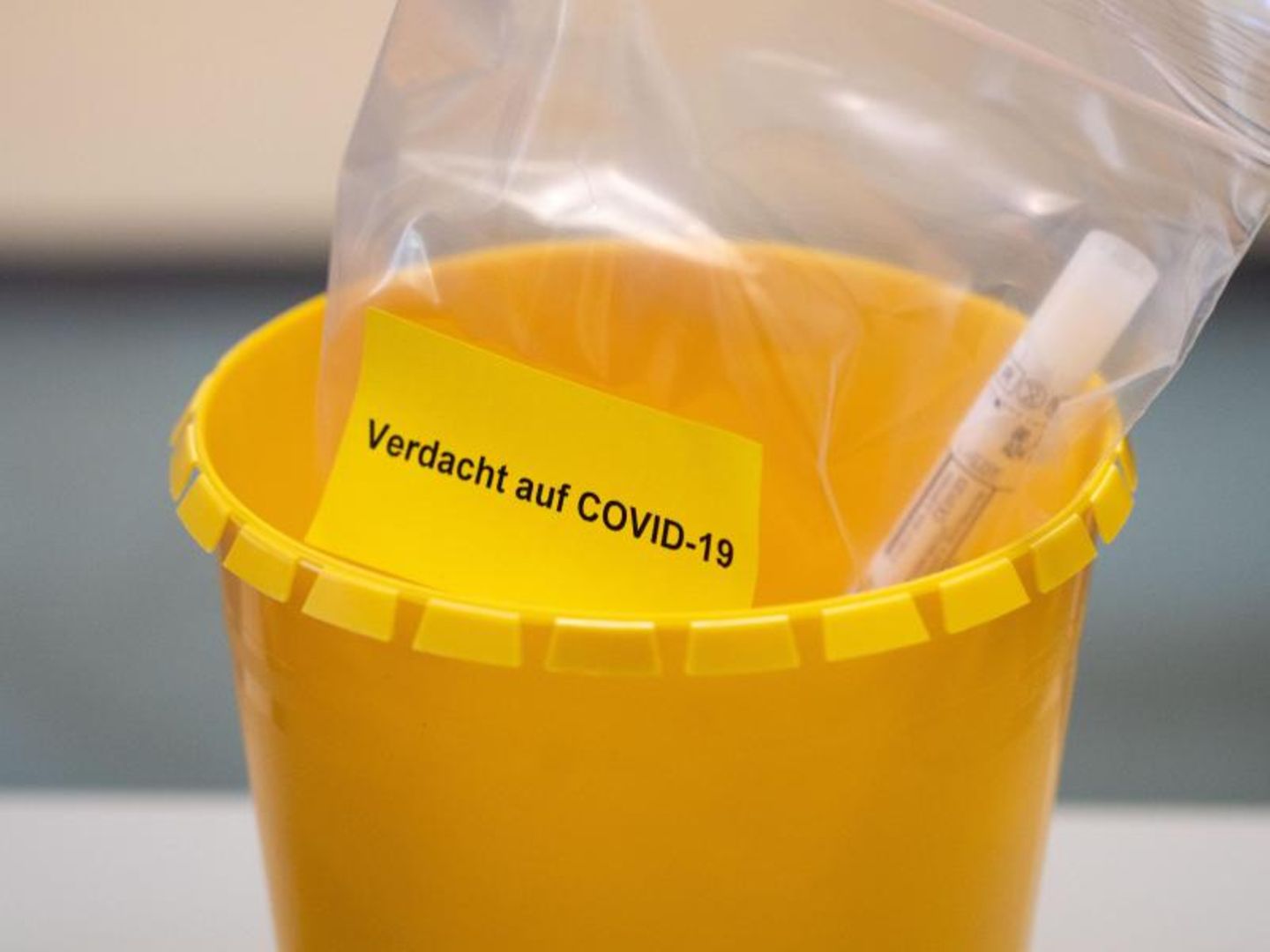 Ein Teströhrchen liegt in einer Tüte mit der Aufschrift "Verdacht auf COVID-19".