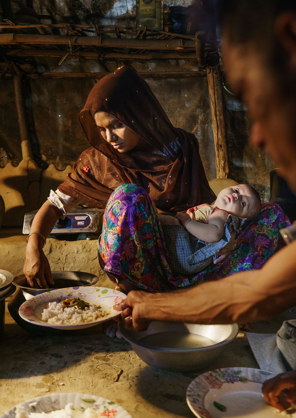 Bangladesch: Die Rohingya Arafa Begum serviert ihrem Mann Essen. Die kargen Vorräte lagern auf einem Holzgestell über dem Gaskocher Bangladesch: Die Rohingya Arafa Begum serviert ihrem Mann Essen. Die kargen Vorräte lagern auf einem Holzgestell über dem Gaskocher