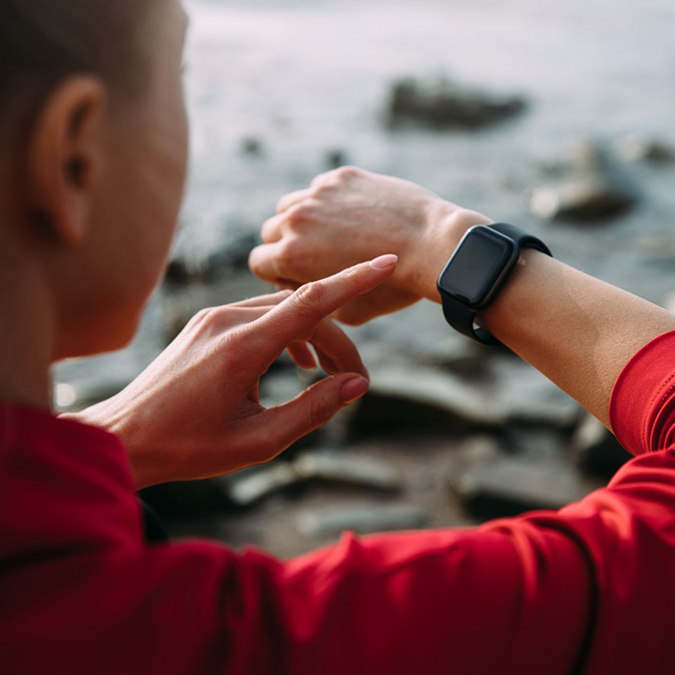Frau schaut auf ihre Smart Watch am Wasser
