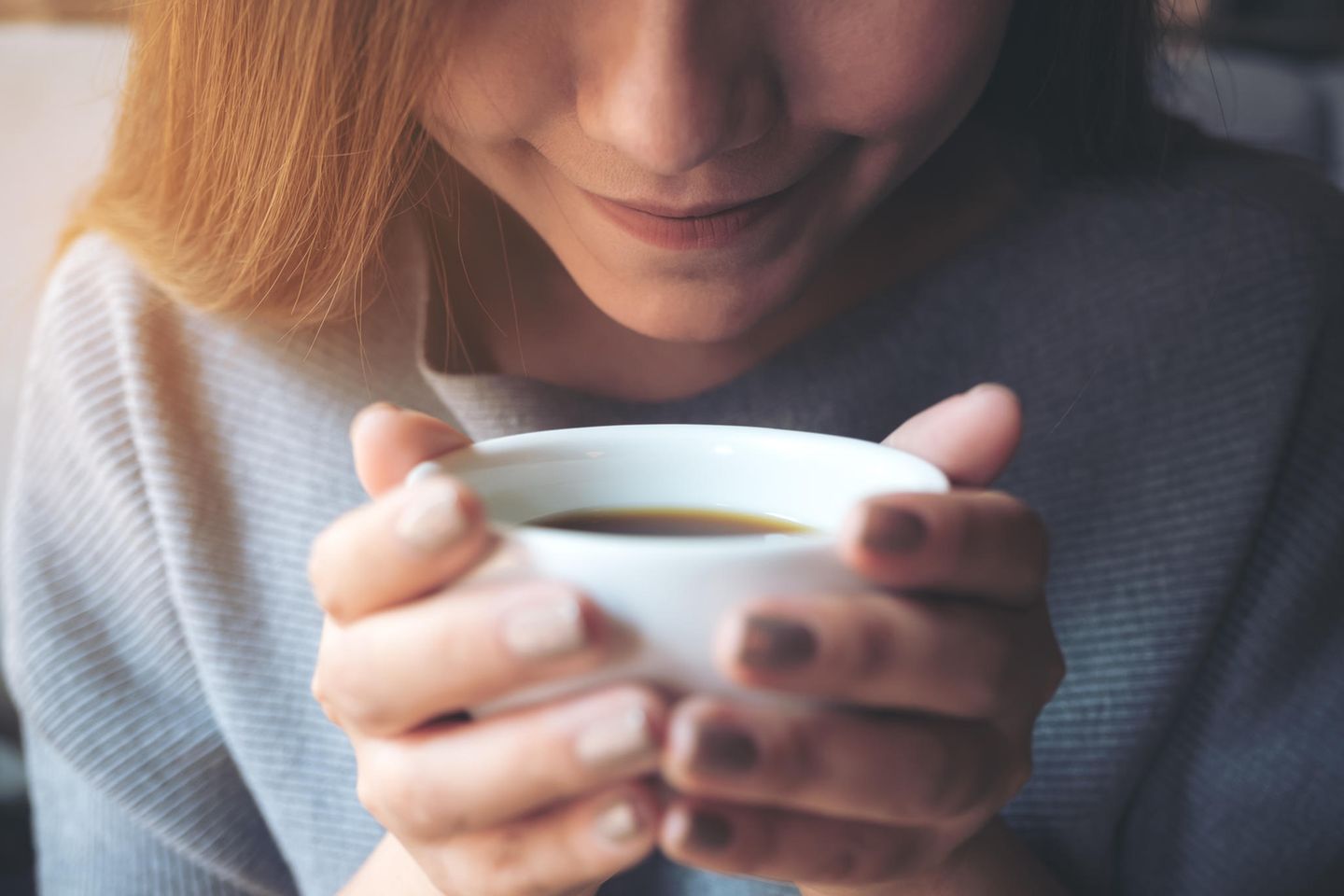 "Kaffee entzieht dem Körper Wasser" Junge Frau genießt den Geruch ihres Kaffees