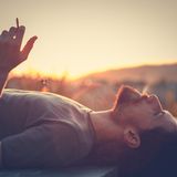 Mann raucht auf dem Rücken liegend eine Zigarette