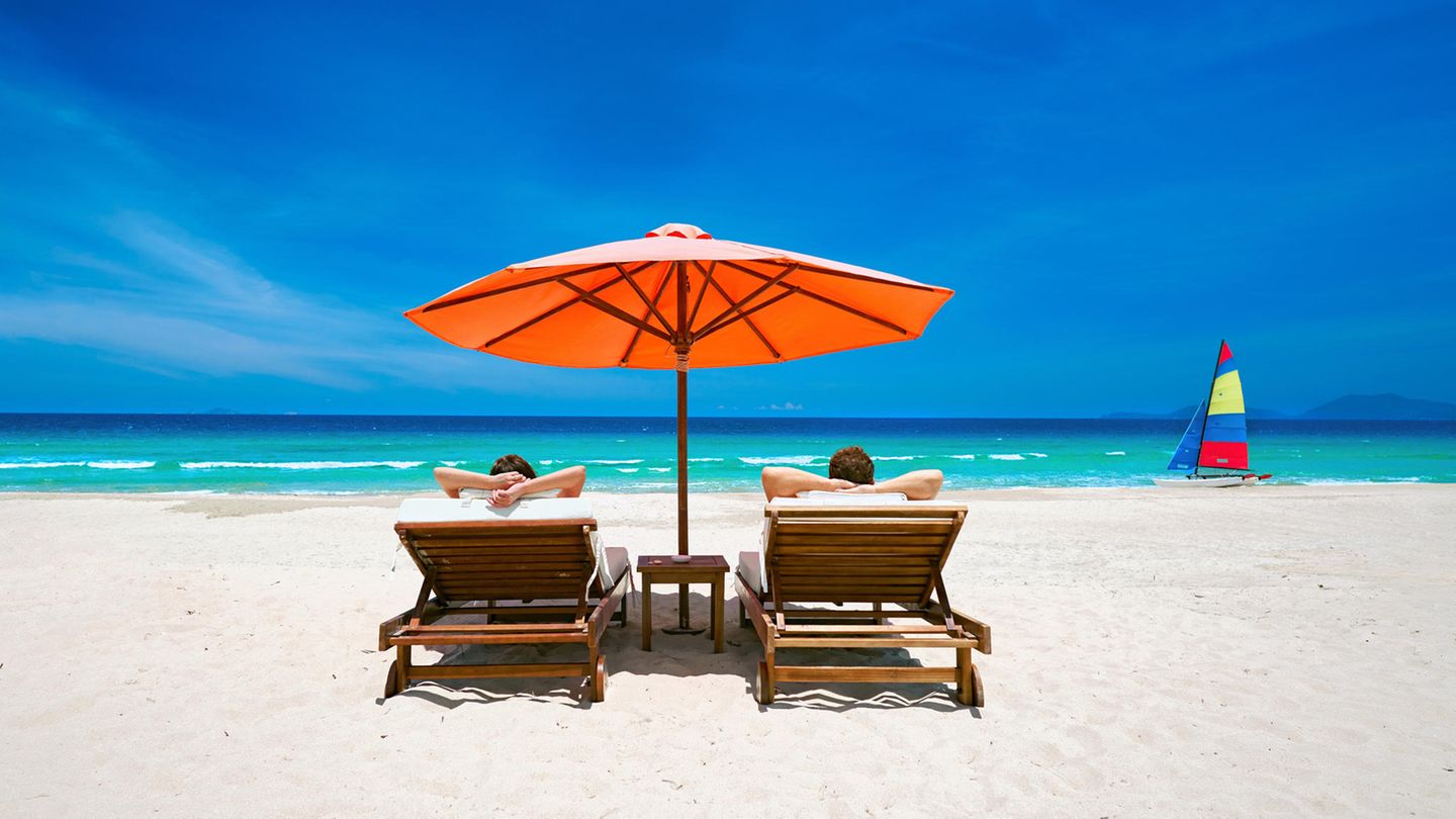 Ein Paar sonnt sich auf Liegen am Strand mit Blick aufs Meer