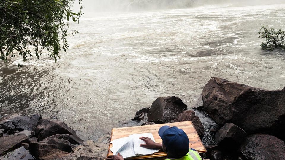Pervious Katyamba, 29, is a security guard and watchman at the boiling pot down the Victoria falls. Since 3 years he is sitting here from 6am to 6pm. Not many tourists go down that steep trail (about 20/day) and they have to sign his register. Sometimes... Unter der Victoria Falls Bridge führt Pervious Katyamba Buch: Jeden Morgen bezieht er seinen Posten am Fluss und bittet die wenigen Besucher, die hier ans Ufer treten, sich in eine Kladde einzutragen, "damit niemand verloren geht". Ein eher einsamer Job