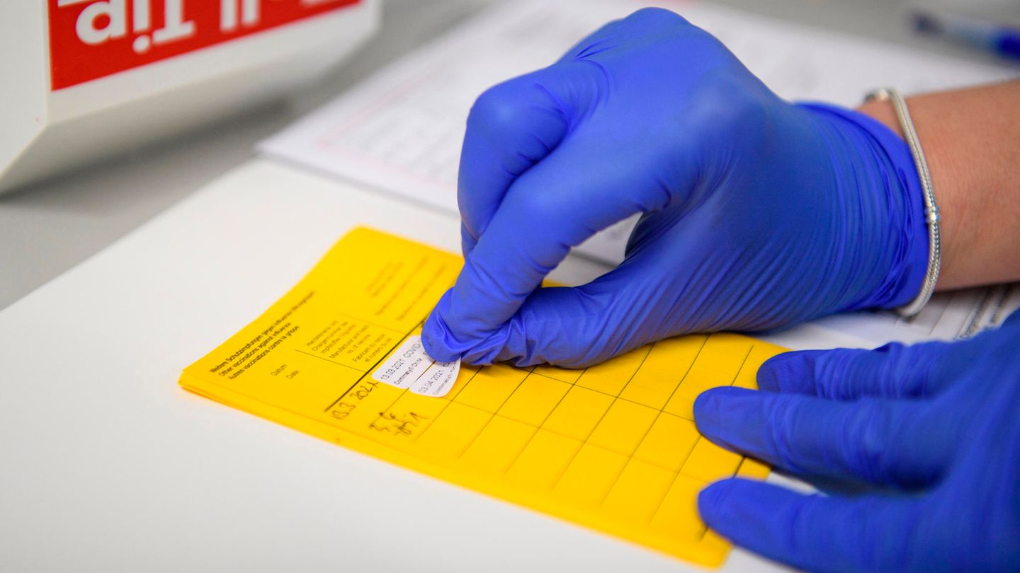 Aufkleber für eine Impfung wird in den gelben Impfpass geklebt