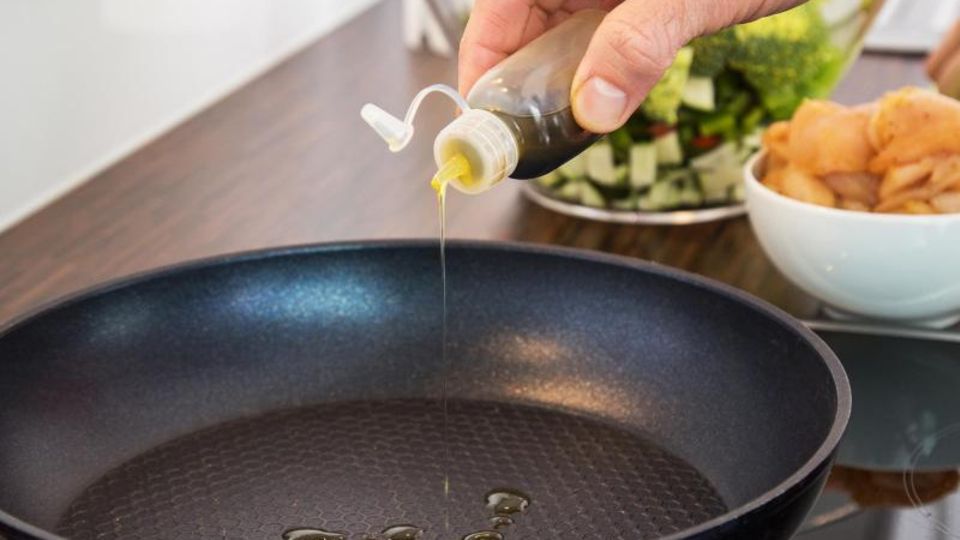 Beim Kochen wird Öl in eine beschichtete Pfanne gegossen Beim Kochen wird Öl in eine beschichtete Pfanne gegossen
