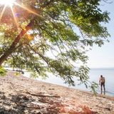 Eine sehr, kleine Straße führt zum Parkplatz am Na de Huk. Hier können nur eine Handvoll Autos stehen, was den möglichen Besucherandrang trotz der Nähe zum Wasser stark einschränkt. Vom Parkplatz aus landet man direkt am Strand, der sich zur Rechten als langes Band am Fördeufer zeigt. Der recht feinsandige Strand zeigt am Spülsaum eventuell einen Mantel aus Algen. Im Wasser selbst treffen die Füße auf kiesige Flächen, sodass Badschuhe sinnvoll sind. Ein paar Meter weiter draußen ist das Wasser extrem klar und perfekt geeignet für längeres Schwimmen. Stand-up-Paddler und Kajaker haben die Möglichkeit, auch die Halbinsel selbst zu erkunden, was wegen der Findlingsansammlung am Ufer zu Fuß extrem mühselig wäre. An der Spitze der Halbinsel hat man als Wassersportler das Privileg, im superklaren Wasser Einblick in die Unterwasserwelt zu bekommen, die hier wegen der bis zu autogroßen Findlinge am Fördeboden äußerst interessant ist.    Als Einrichtung finden wir am Parkplatz nur ein Trockenklosett. Wenn sich der Hunger meldet, stößt man am anderen Ende des Strandes beim Campingplatz auf das Restaurant "Zum Schwarzen Raben". 