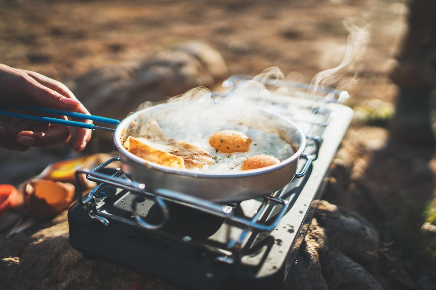 Person brät Eier auf einem Campingkocher