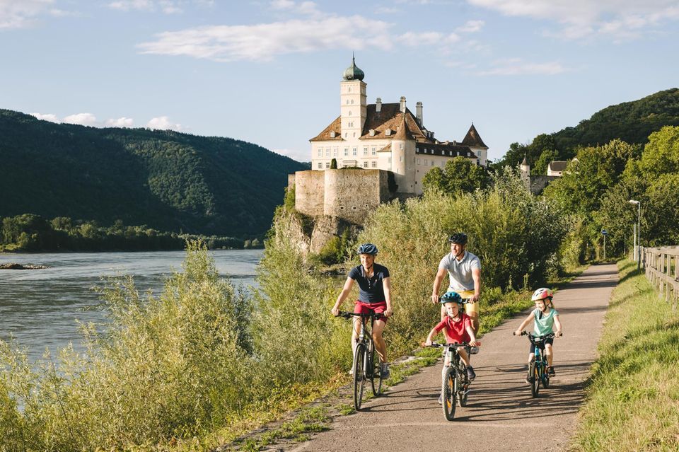 Eine Familie radelt auf dem Donauradweg an Schloss Schönbiel vorbei Eine Familie radelt auf dem Donauradweg an Schloss Schönbiel vorbei
