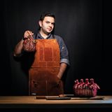 Küchenchef Mateo hält ein Beil und ein Stück Fleisch in der Hand