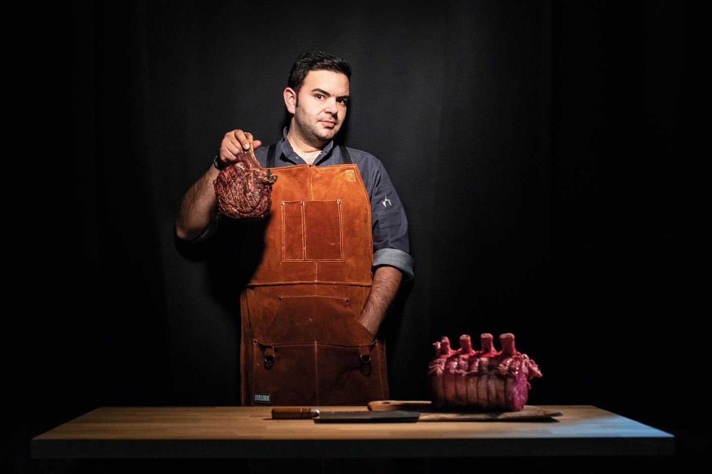 Küchenchef Mateo hält ein Beil und ein Stück Fleisch in der Hand