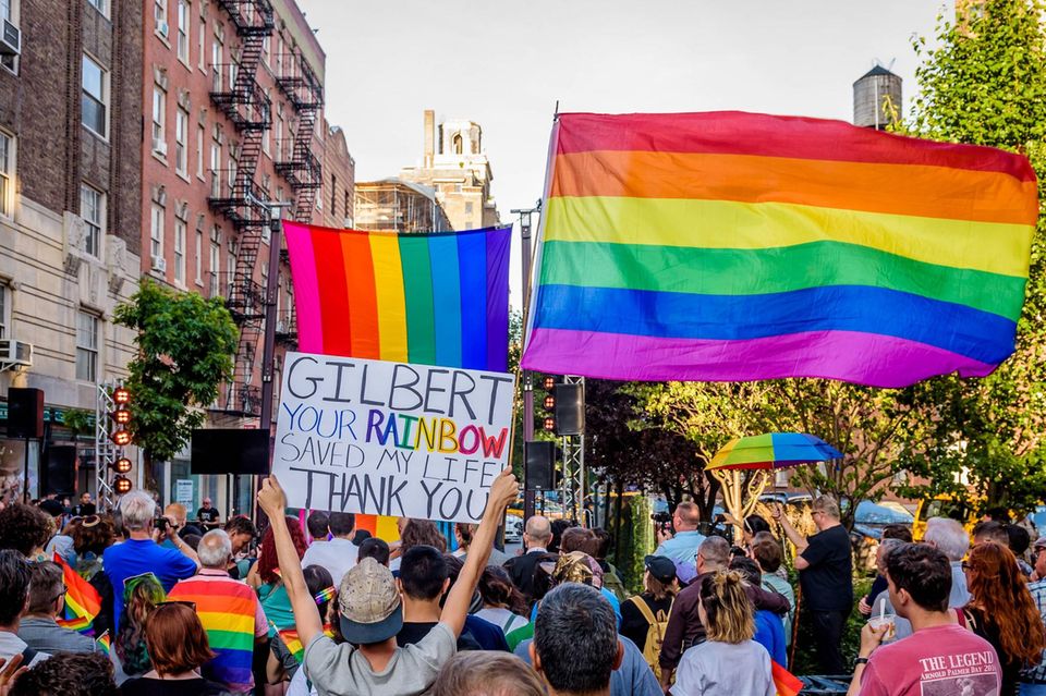 Menschen auf einem Christopher Street Day schwenken die Regenbogenflagge