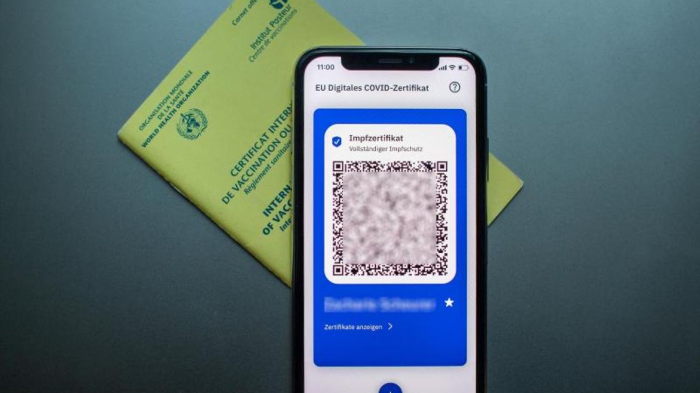 Impfpass un digitaler Impfpass auf dem Handy liegen auf dem Tisch