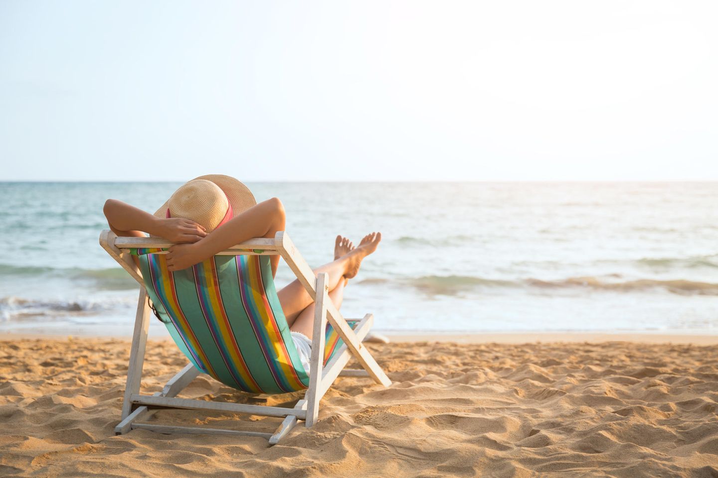 Frau mit Sonnenhut entspannt im Liegenstuhl am Strand