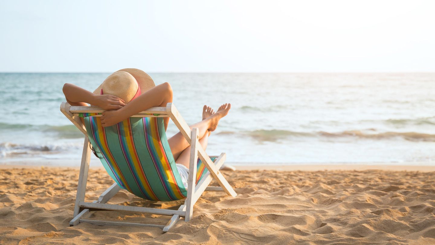Frau mit Sonnenhut entspannt im Liegenstuhl am Strand
