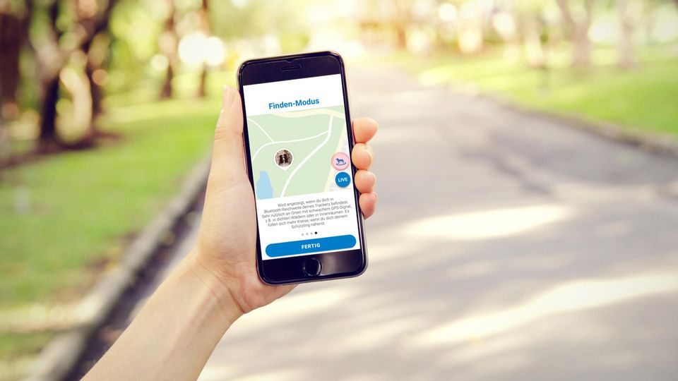 Frau hält ihr Smartphone mit der App "Tractive" draußen in der Hand