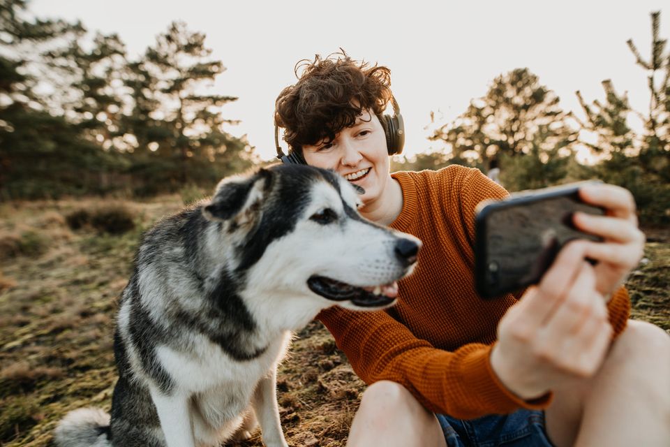 Junge Frau und Hund sitzen in der Natur und schauen auf ein Smartphone