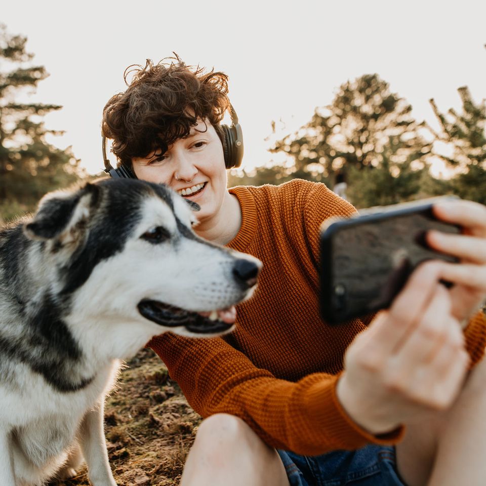 Junge Frau und Hund sitzen in der Natur und schauen auf ein Smartphone