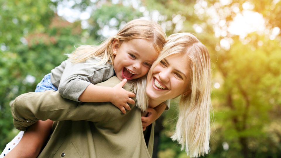 Lachende Mutter hält Tochter auf dem Rücken