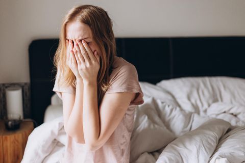 Junge Frau sitzt im Bett und fühlt sich krank