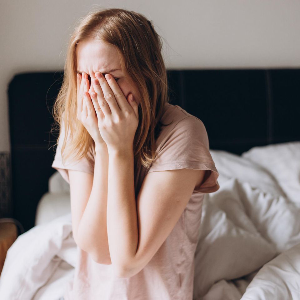 Junge Frau sitzt im Bett und fühlt sich krank