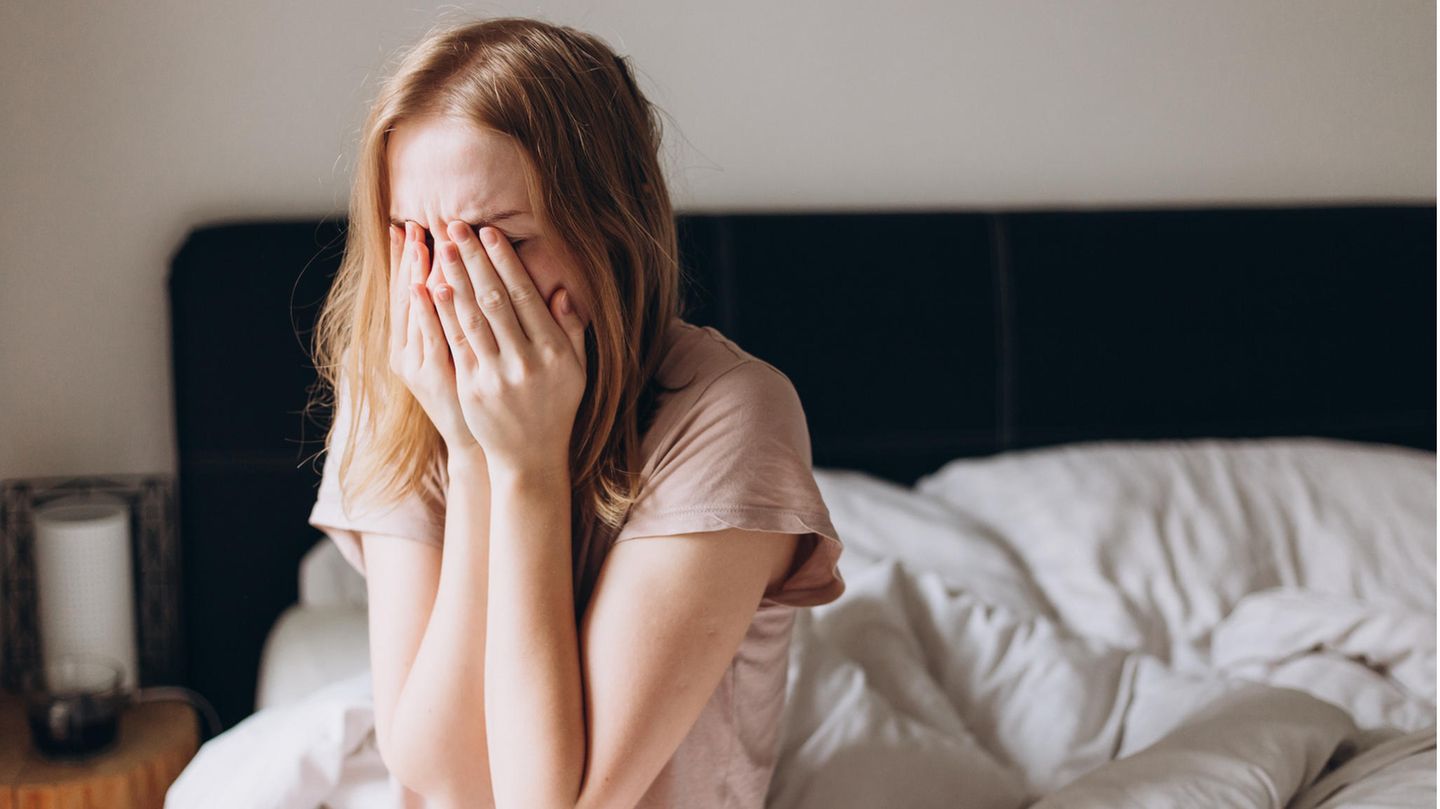 Junge Frau sitzt im Bett und fühlt sich krank