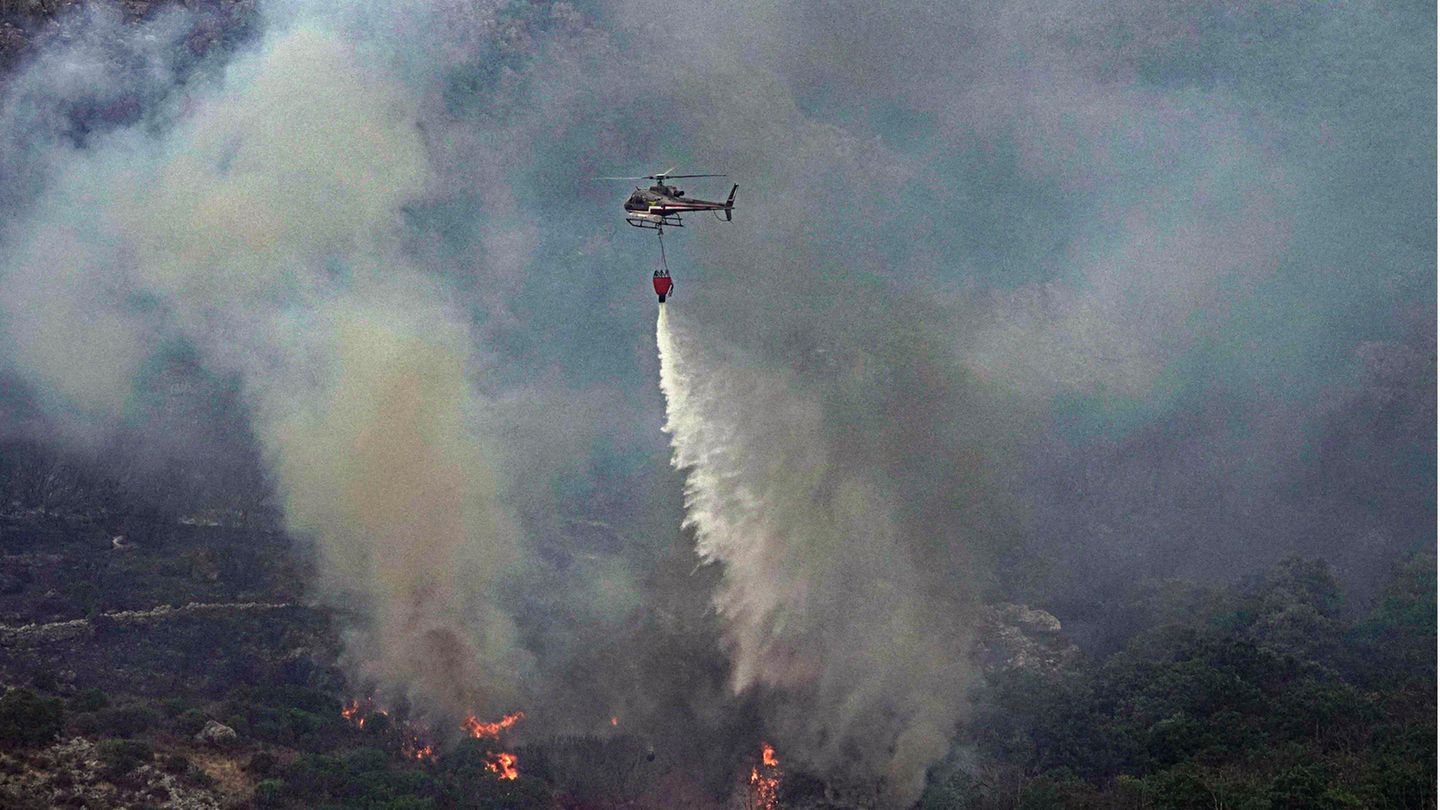 Ein Hubschrauber wirft über einem Waldgebiet in Cugliari Wasser ab, um Flammen zu löschen
