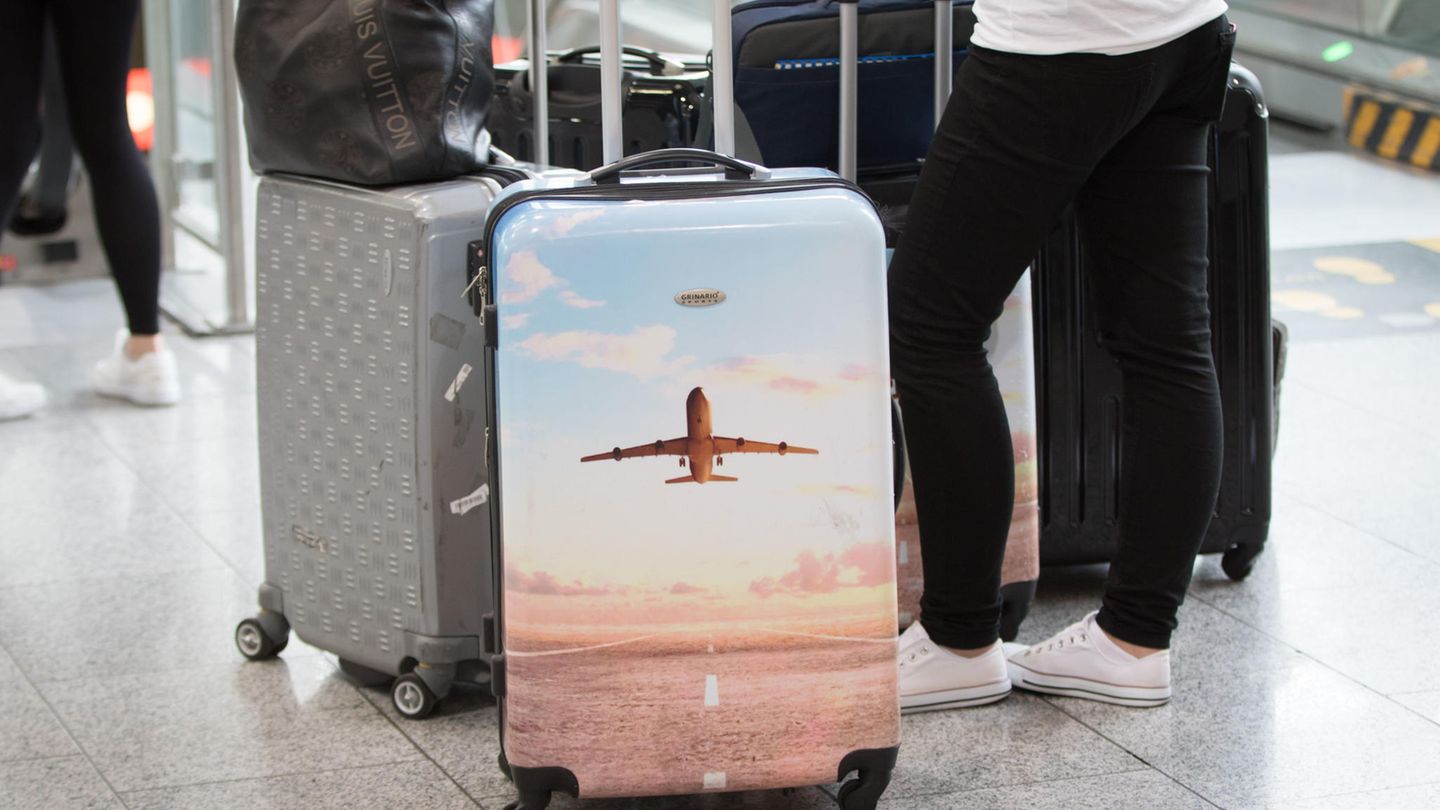 Urlauberinnne und Urlauber stehen mit dem Koffer am Flughafen