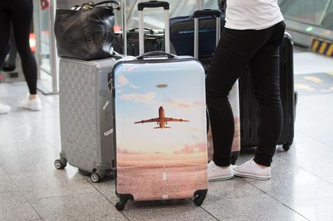 Urlauberinnne und Urlauber stehen mit dem Koffer am Flughafen