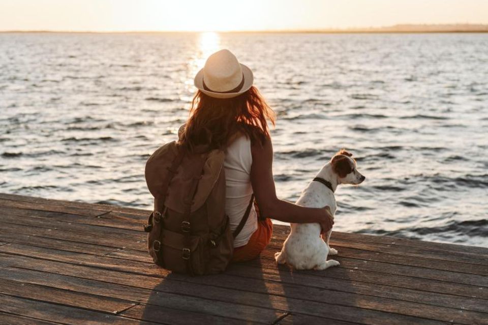 Frau sitzt mit ihrem Hund euf einem Steg und schaut in die Ferne