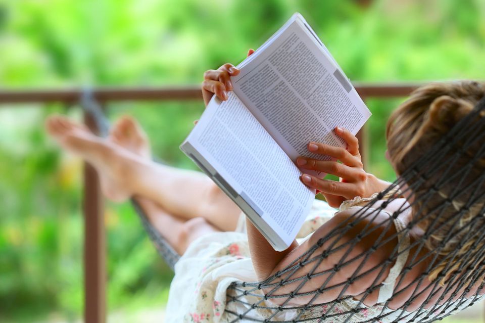 Frau liest in einer Hängematte ein Buch