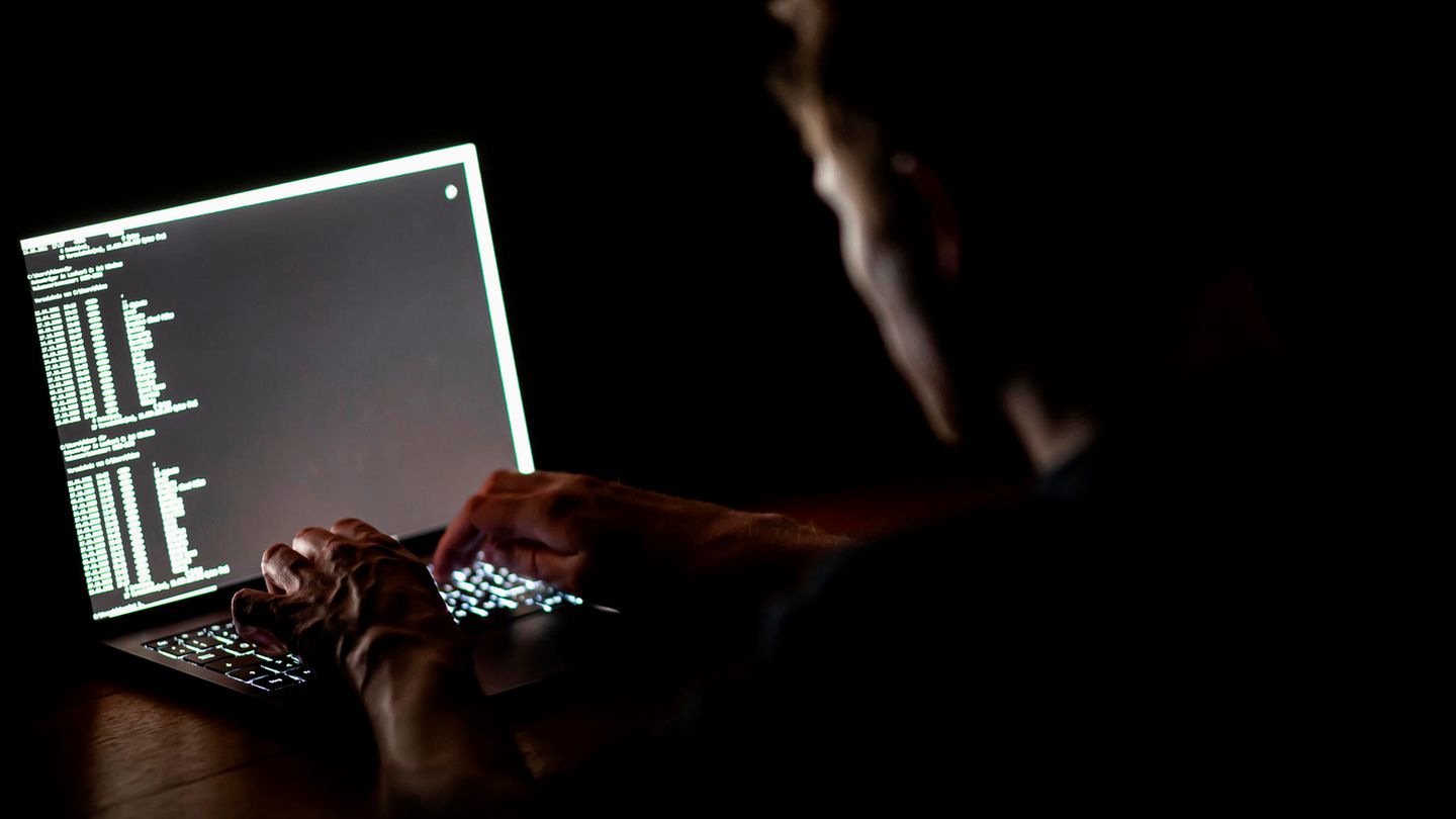 Ein Mann schreibt auf der Tastatur eines Laptops im Dunkeln