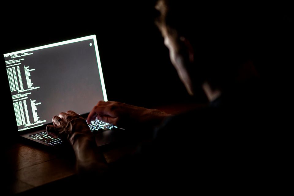 Ein Mann schreibt auf der Tastatur eines Laptops im Dunkeln