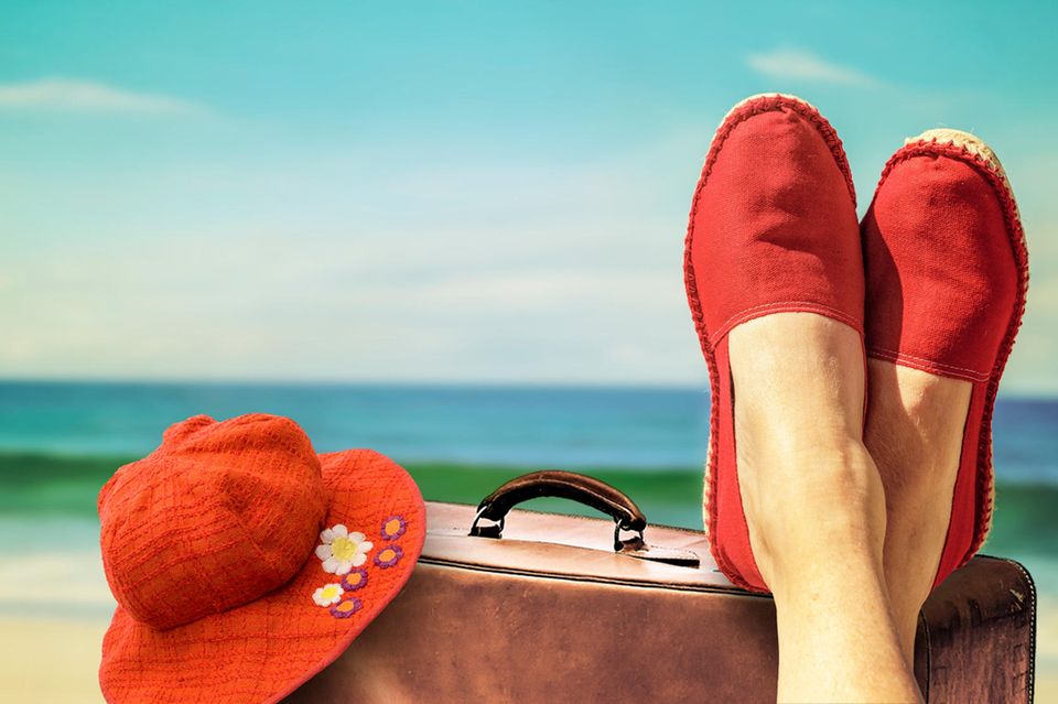 Frau legt ihre Füße auf einen Koffer am Strand