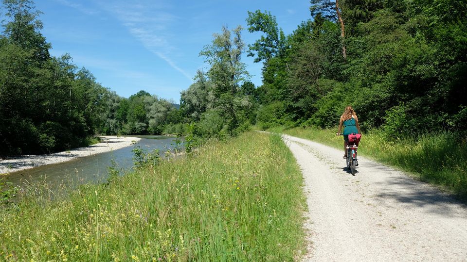 Frau fährt bei Sonnenschein am Ufer der Ammer auf dem Rad entlang