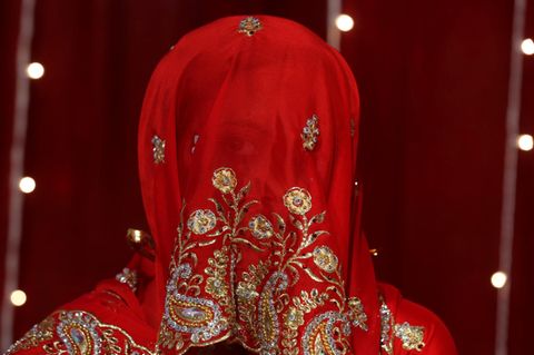 Eine indische Braut blickt durch ihren roten Schleier
