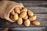 Frische Kartoffeln auf altem Sack auf Holzhintergrund