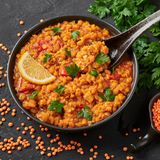 Rote Linsen in einer schwarzen Schüssel auf dunklem Schiefer Tischplatte und Linsengericht in einer Pfanne