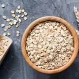 Haferflocken in einer Holzschüssel mit Weizenähren vor grauem Hintergrund