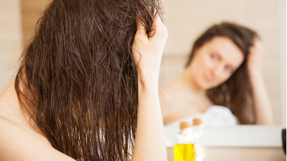 Junge Frau trägt vor einem Spiegel eine Ölmaske auf das Haar auf