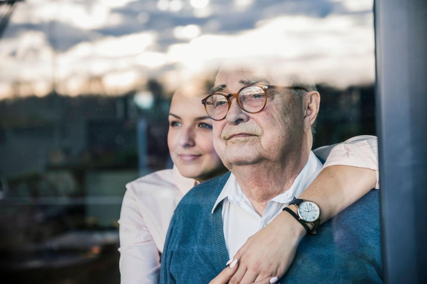Frau umarmt ihren Vater und beide schauen aus dem Fenster