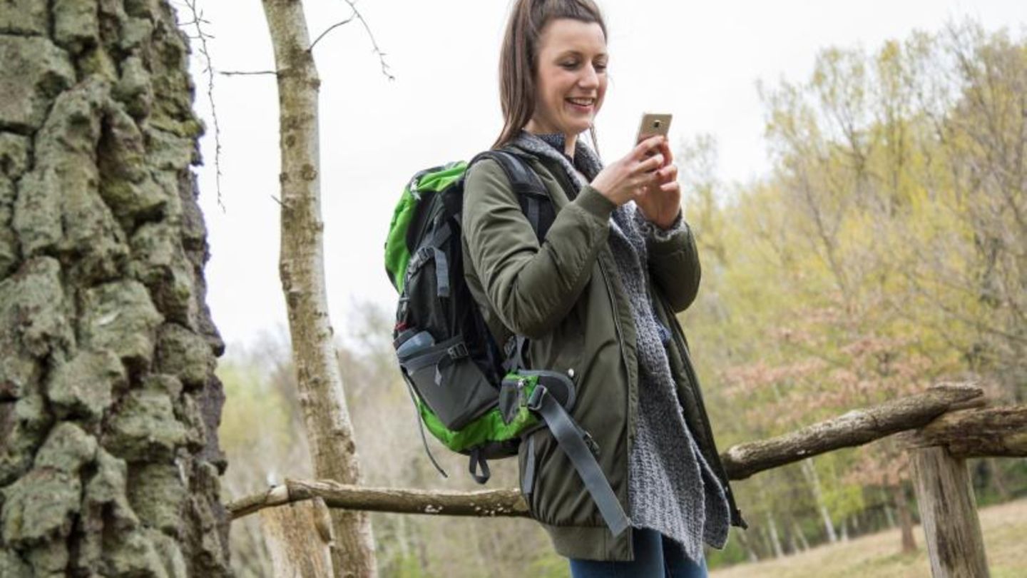 Frau schaut beim Wandern auf ihr Smartphone
