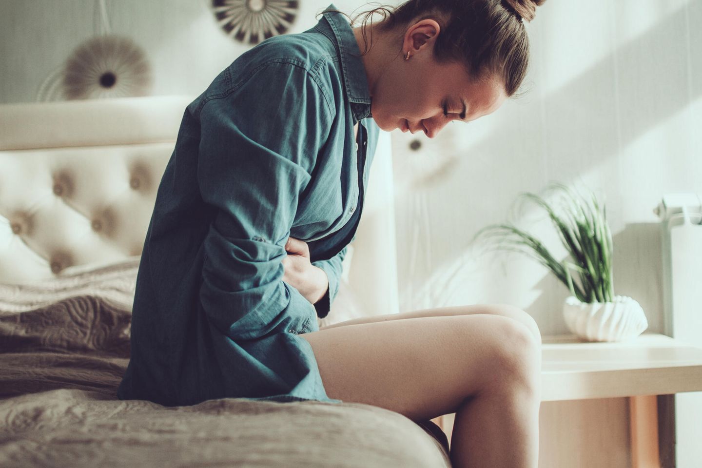 Junge Frau, die unter Menstruationsschmerzen leidet, sitzt auf der Bettkante