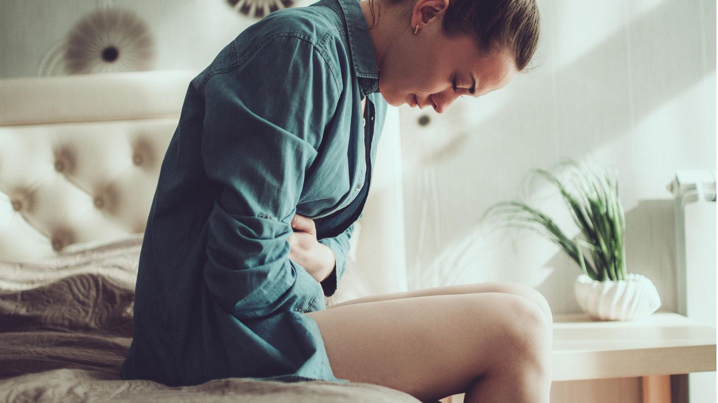 Junge Frau, die unter Menstruationsschmerzen leidet, sitzt auf der Bettkante